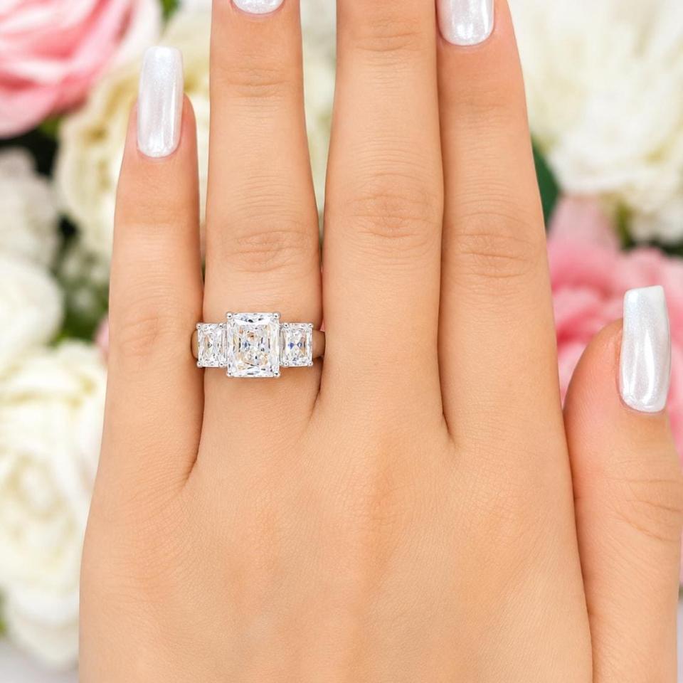 A woman's hand wearing a sterling silver 3-stone engagement ring featuring a 10x8mm radiant cut cubic zirconia center stone with two smaller radiant CZ side stones. The highly polished wide band tapers for comfort. Model image for size and styling reference — not a photo of the actual ring.