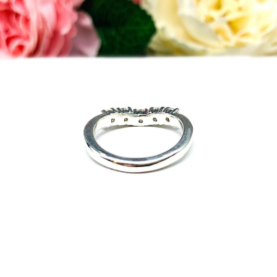 Sterling silver 5-stone curved wedding band featuring 3mm round precision faceted moissanite stones in prong settings, displayed against a soft floral background.