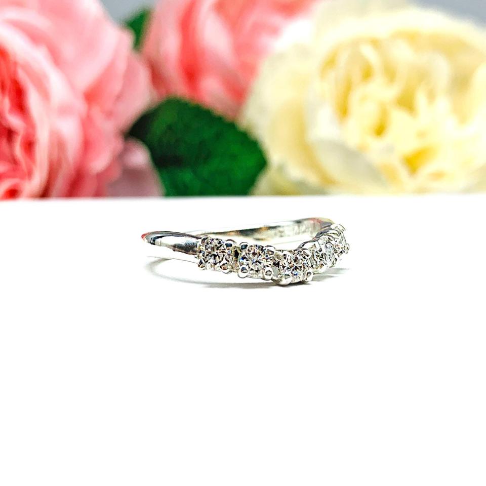 Sterling silver 5-stone curved wedding band featuring 3mm round precision faceted moissanite stones in prong settings, displayed against a soft floral background.