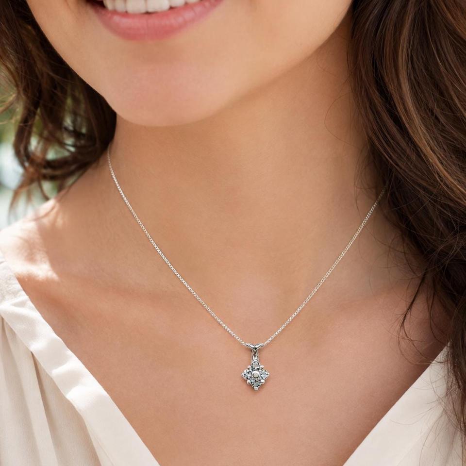 A woman wearing a sterling silver cluster pendant featuring four 3mm round light blue aquamarine gemstones and an elegant twist design bail. Suspended from a delicate sterling silver chain. Model image for size and styling reference — not a photo of the actual necklace.