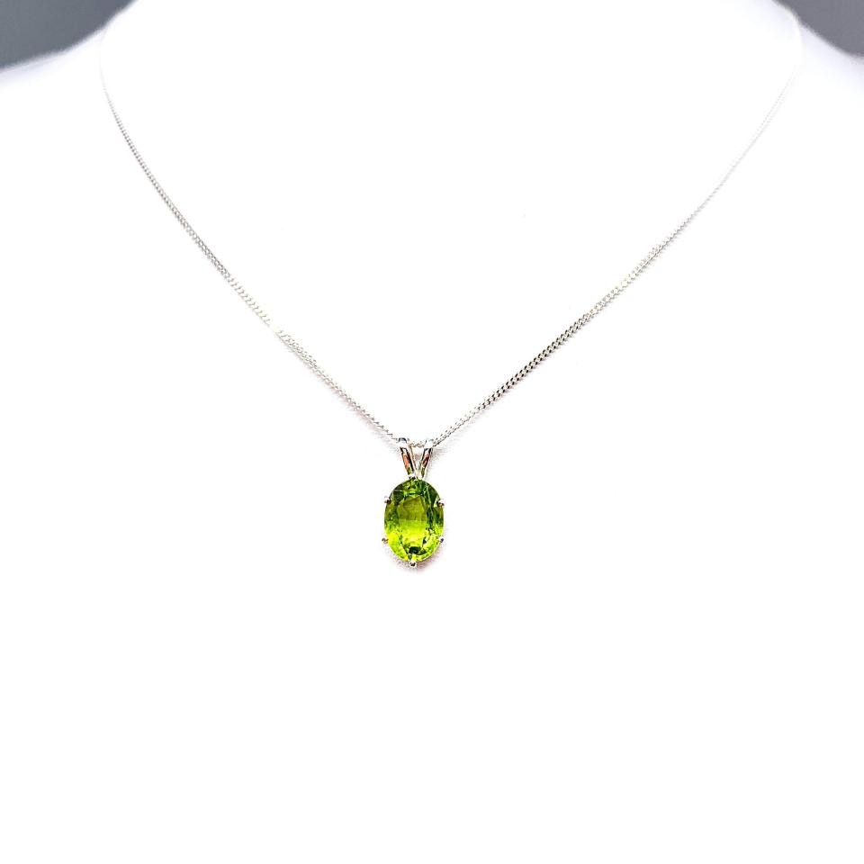 Bright neon green 9×7 mm oval apatite gemstone in a sterling silver six‑prong pendant, suspended from a delicate chain and displayed on a white background.