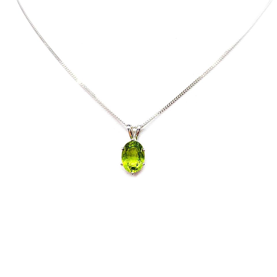 Bright neon green 9×7 mm oval apatite gemstone in a sterling silver six‑prong pendant, suspended from a delicate chain and displayed on a white background.