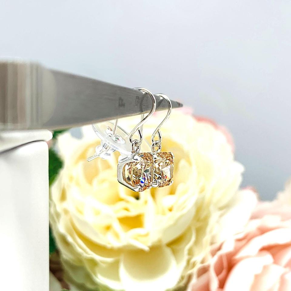 A pair of sterling silver 4-prong dangle earrings with cushion cut champagne cubic zirconia stones. Each dangle is suspended from a thin earwire that comes with a silicone back.