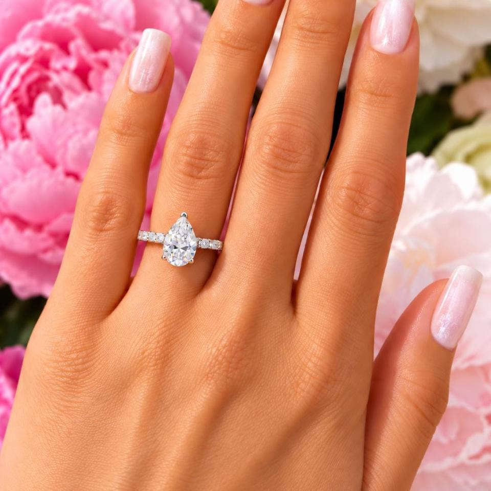 A woman's hand wearing an elegant sterling silver engagement ring set featuring a 10x7mm precision-cut pear cubic zirconia with pave CZ accents in a half eternity band. Model image for size and styling reference — not a photo of the actual ring.