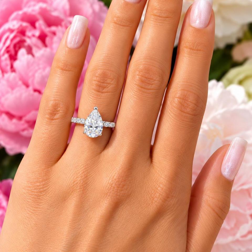 A woman's hand wearing an elegant sterling silver engagement ring set featuring a 12x8mm precision-cut pear cubic zirconia with pave CZ accents in a half eternity band. Model image for size and styling reference — not a photo of the actual ring.