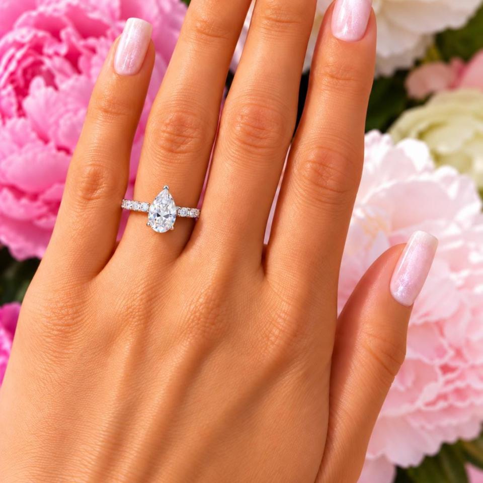 A woman's hand wearing an elegant sterling silver engagement ring set featuring a 9x6mm precision-cut pear cubic zirconia with pave CZ accents in a half eternity band. Model image for size and styling reference — not a photo of the actual ring.