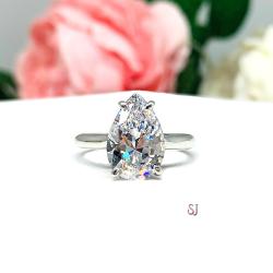 Elegant 4-prong sterling silver cathedral engagement ring set featuring a 12x8mm precision-cut pear cubic zirconia.  Displayed on a white surface with soft pastel floral background.