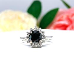Sterling silver engagement ring with a round 5mm–8mm black moissanite center stone, encircled by a halo of small colorless moissanites in a floral-inspired setting, shown with soft floral background.