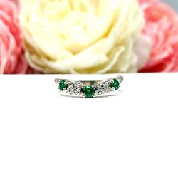 Sterling silver five-stone curved wedding band with three 3mm round lab-created emeralds and two 3mm round DEF moissanites, shown against a soft floral background.