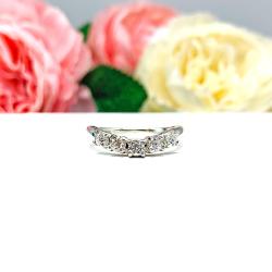 Sterling silver 5-stone curved wedding band featuring 3mm round precision faceted moissanite stones in prong settings, displayed against a soft floral background.