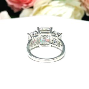 Sterling silver 3-stone engagement ring featuring an 8x6mm-10x8mm radiant cut cubic zirconia center stone with two smaller radiant CZ side stones. The highly polished wide band tapers for comfort. Displayed on a white surface with soft floral background.