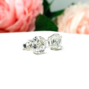 A pair of silver basket earrings set with oval natural white topaz gemstones. Each earring is displayed on a white background and set slightly to the right and shows the butterfly friction clasps.