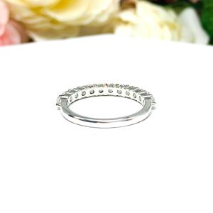 Sterling silver band with 12 round 2.5mm white topaz gemstones set in a shared prong setting. The band is on a white surface with pink and white flowers in the background.