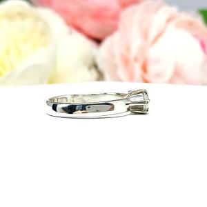 A 6-prong sterling silver, horizontal east west set engagement ring featuring a precision-faceted near colorless (G/H color) marquise cubic zirconia.  Displayed on a white surface with soft pastel floral background.