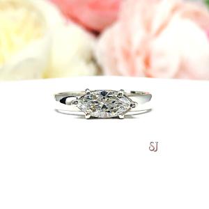 A 6-prong sterling silver, horizontal east west set engagement ring featuring a precision-faceted near colorless (G/H color) marquise cubic zirconia.  Displayed on a white surface with soft pastel floral background.