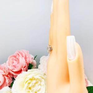 Mannequin hand with long white shimmery nails, displayed against a soft white-gray background with pink and white floral accents. The hand is wearing a sterling silver ring with an oval lab created white sapphire set in a 6-prong setting.
