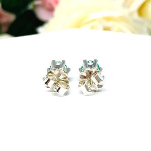 A pair of silver 6 prong earrings set with 6mm round sea foam green lab spinels, displayed with both earrings facing to towards the back to showcase the centrally located posts and butterfly friction clasps. The earrings are shown on a white background.