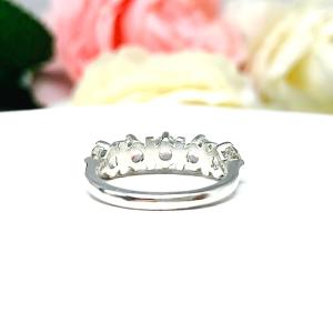 A sterling silver ring featuring five 4mm round white topaz gemstones in a row. The ring has rounded bars separating each stone. Displayed on a white surface with pastel floral background.
