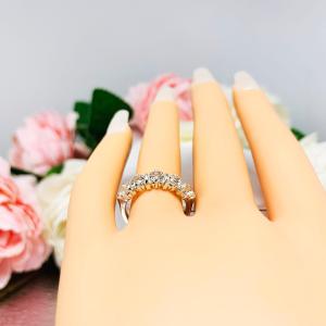 Mannequin hand with long white shimmery nails, displayed against a soft white-gray background with pink and white floral accents. The hand is wearing a sterling silver ring featuring five 4mm round white topaz gemstones in a row. The ring has rounded bars separating each stone.