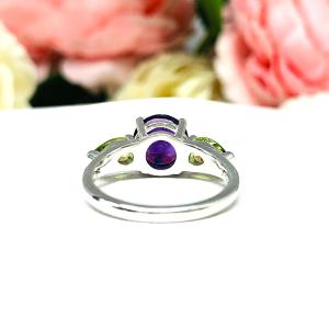 Sterling silver ring featuring a vibrant 8mm round African amethyst flanked by two pear-cut peridot side stones. The rich purple and bright green gemstones create a striking contrast, set against a soft floral background that enhances the ring’s natural elegance.