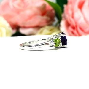 Sterling silver ring featuring a vibrant 8mm round African amethyst flanked by two pear-cut peridot side stones. The rich purple and bright green gemstones create a striking contrast, set against a soft floral background that enhances the ring’s natural elegance.