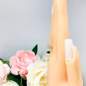 Mannequin hand with long white shimmery nails, displayed against a soft white-gray background with pink and white floral accents. The hand is wearing a sterling silver split-prong cathedral engagement ring set with a near colorless old mine cut cubic zirconia.