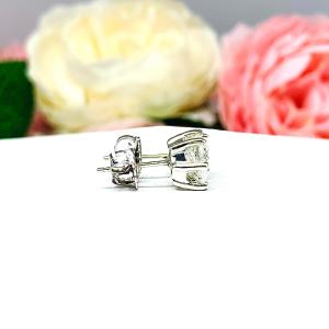 A pair of 10k white gold stud earrings set with oval brilliant cut moissanites.  The 6 prong earrings are on a white surface with both earrings facing to the right to showcase center post and butterfly friction clasps.