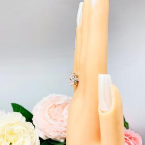 Mannequin hand with long white shimmery nails, displayed against a soft white-gray background with pink and white floral accents. The hand is wearing an elegant sterling silver cathedral engagement ring set with a large radiant cut cubic zirconia.