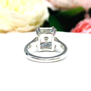 Elegant sterling silver cathedral engagement ring set with a large radiant cut cubic zirconia, beautifully photographed against a romantic and timeless soft-focus floral background of pink and white blooms.