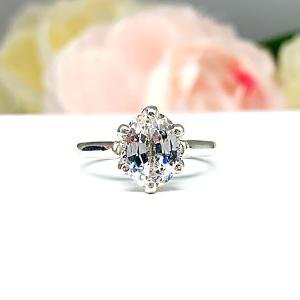 Sterling silver engagement ring with an oval lab created white sapphire set in a 6-prong tulip design setting set against a white surface with soft-focus pink and white flowers in the background.