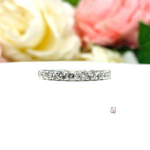 Sterling silver band with 12 round 2.5mm white topaz gemstones set in a shared prong setting. The band is on a white surface with pink and white flowers in the background.