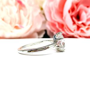 Sterling silver ring with an oval lab created white sapphire set in a 6-prong setting set against a white surface with soft-focus pink flowers in the background.