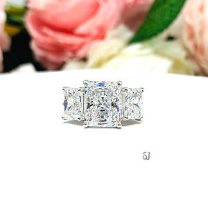 Sterling silver 3-stone engagement ring featuring an 8x6mm-10x8mm radiant cut cubic zirconia center stone with two smaller radiant CZ side stones. The highly polished wide band tapers for comfort. Displayed on a white surface with soft floral background.