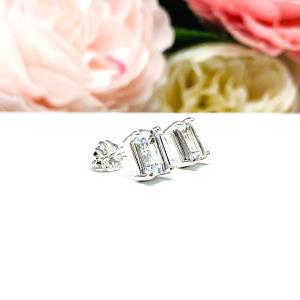 A pair of silver earrings set with emerald cut natural white topaz gemstones. Each earring is displayed on a white background and set slightly to the right and shows the butterfly friction clasps.