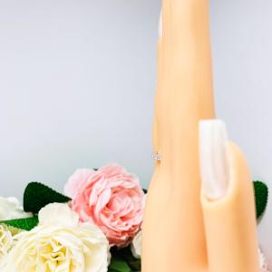 Mannequin hand with long white shimmery nails, displayed against a soft white-gray background with pink and white floral accents. The hand is wearing a sterling silver half-eternity, stackable 7-stone wedding band featuring 2mm round precision faceted cubic zirconia stones in prong settings.