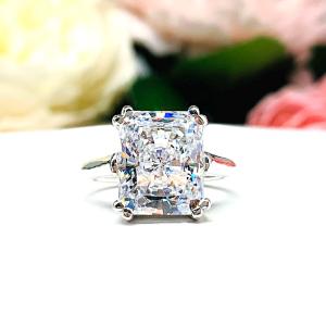 Elegant sterling silver cathedral engagement ring set with a large radiant cut cubic zirconia, beautifully photographed against a romantic and timeless soft-focus floral background of pink and white blooms.