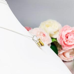 A sterling silver necklace with a pendant featuring a 12x10mm oval-cut, golden citrine gemstone. The necklace is resting against a white background.