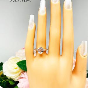 Mannequin hand with long white shimmery nails, displayed against a soft white-gray background with pink and white floral accents. The hand is wearing a sterling silver ring with a 9x7mm oval lab created white sapphire set in a 6-prong setting.
