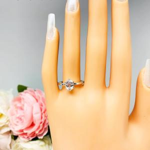Mannequin hand with long white shimmery nails, displayed against a soft white-gray background with pink and white floral accents. The hand is wearing a sterling silver ring with an 8x6mm oval lab created white sapphire set in a 6-prong setting.