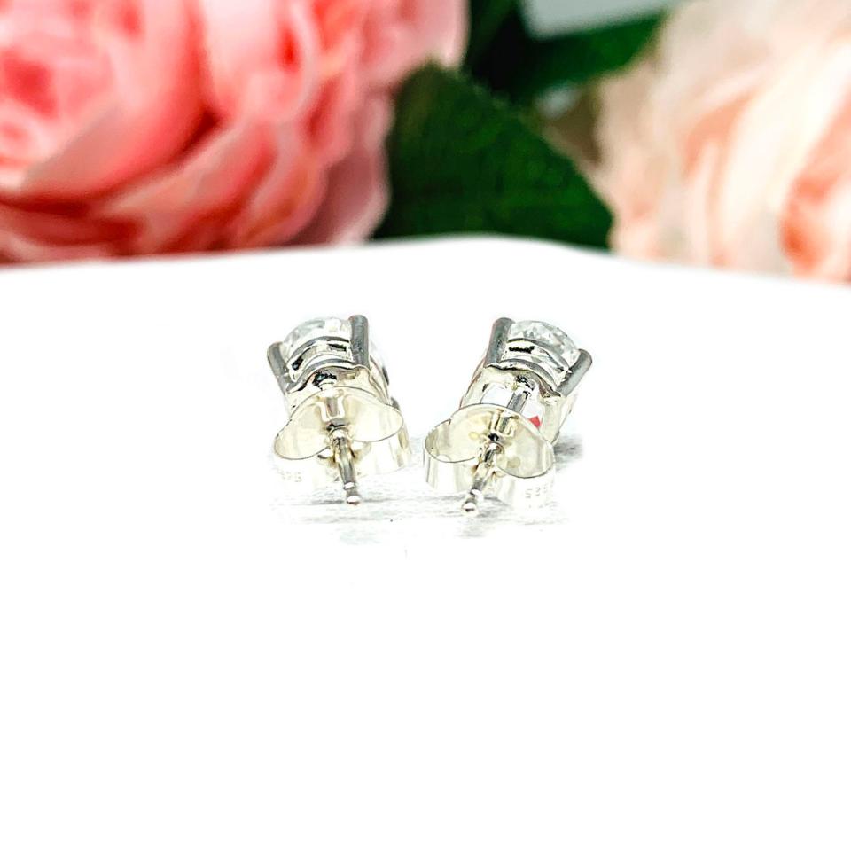 A pair of silver basket earrings set with oval natural white topaz gemstones. The earrings, sitting on a white background, are displayed facing toward the back to show that the posts sit at the top and the butterfly friction backs.