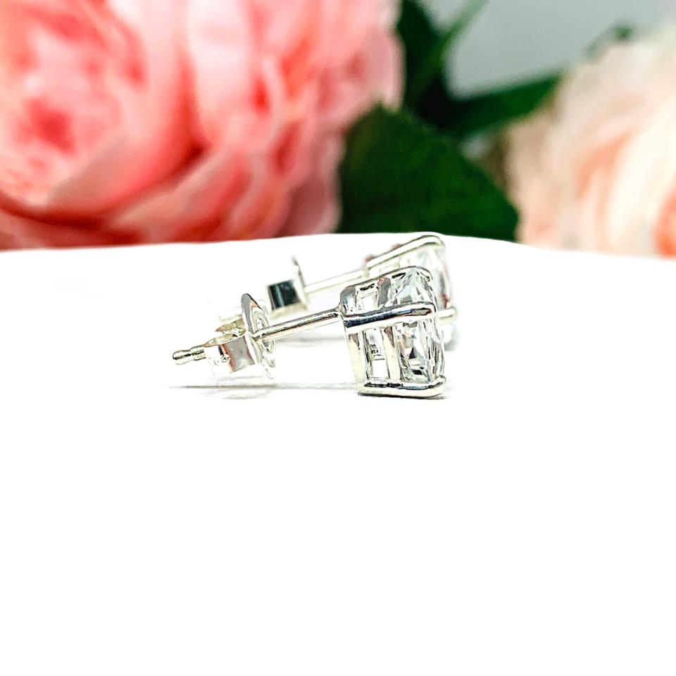 A pair of silver basket earrings set with oval natural white topaz gemstones. Each earring is is sitting on a white background and displayed facing to the right to show that the post sits at the top of the earring and the butterfly friction clasps.
