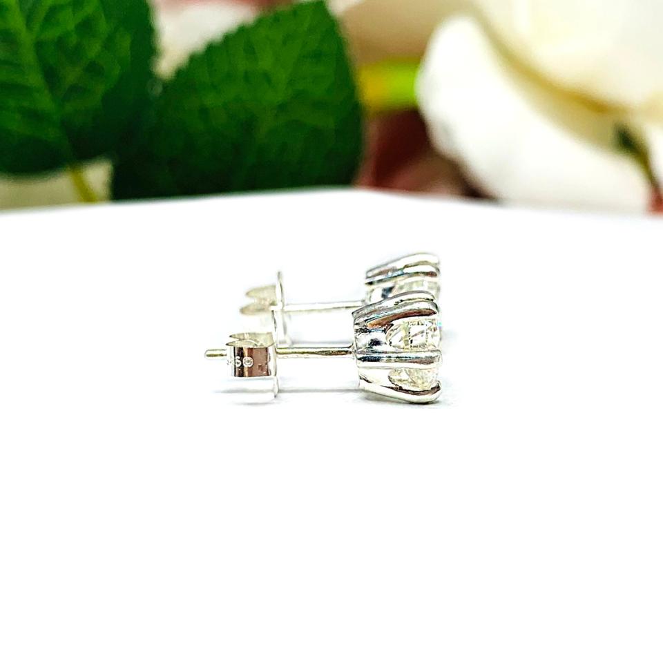 A pair of silver stud earrings set with round brilliant cut 'near colorless or 'G color' cubic zirconias.  The 6 prong earrings are on a white surface with both earrings facing to the right to showcase center post and butterfly friction clasps.