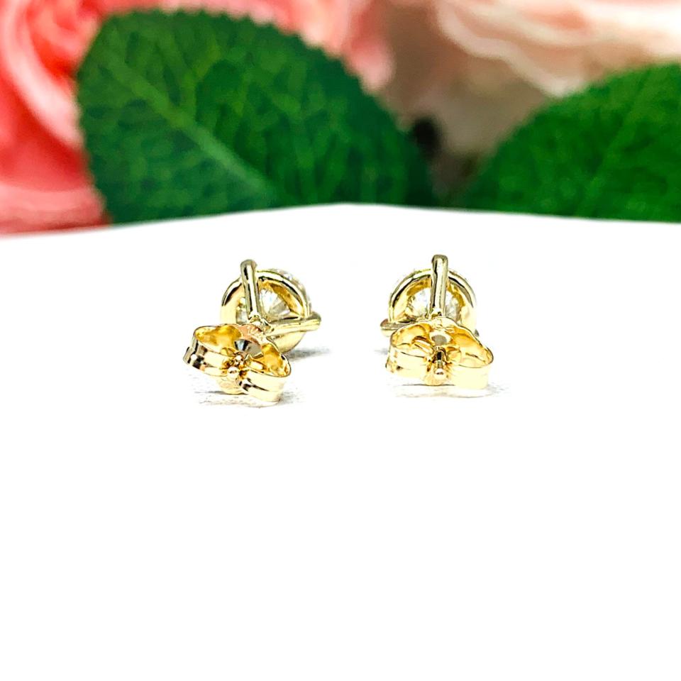 A pair of yellow gold martini stud earrings with round brilliant moissanites. The earrings are on a white background with both earrings facing toward the back to showcase the center post and butterfly friction clasp.