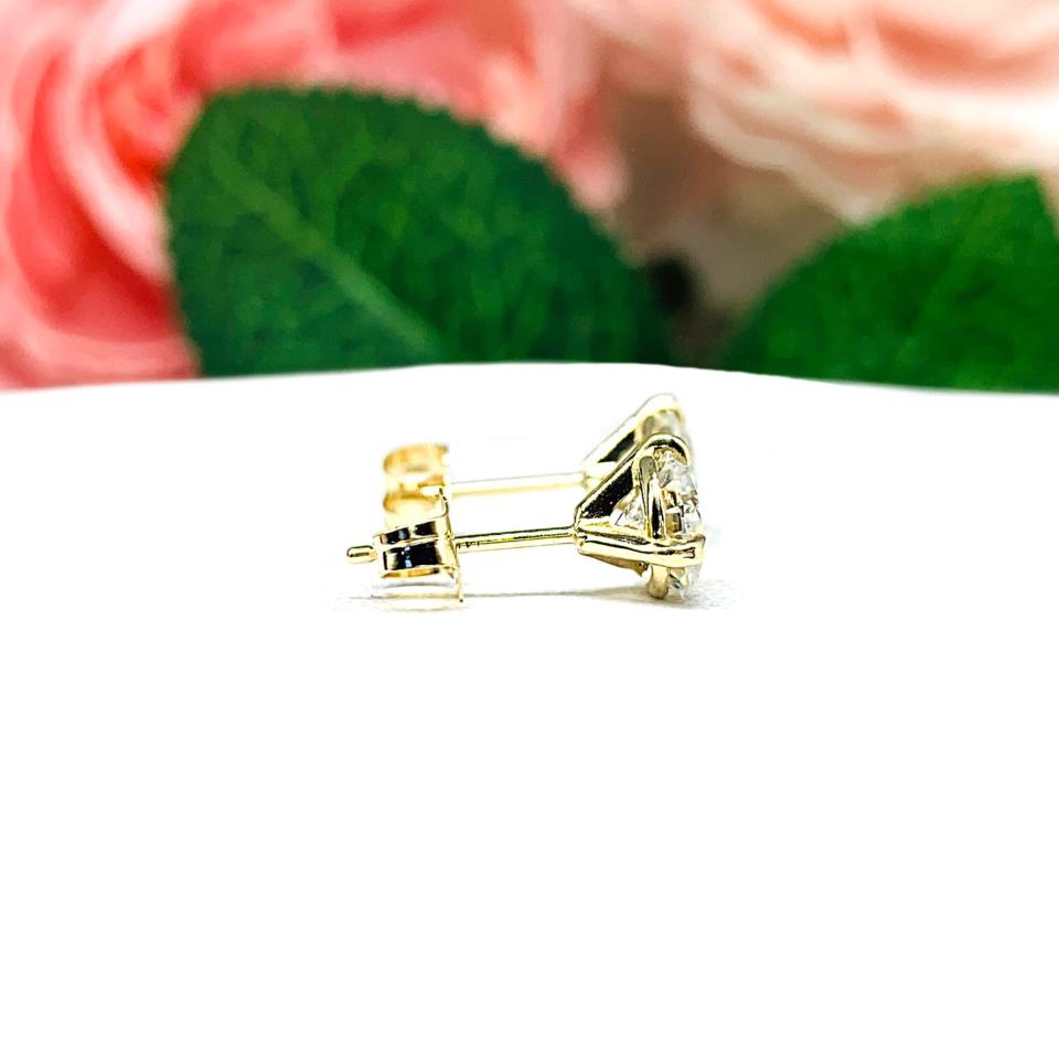 A pair of yellow gold martini stud earrings with round brilliant moissanites. The earrings are on a white background with both earrings facing to the right to showcase the center post and butterfly friction clasp.