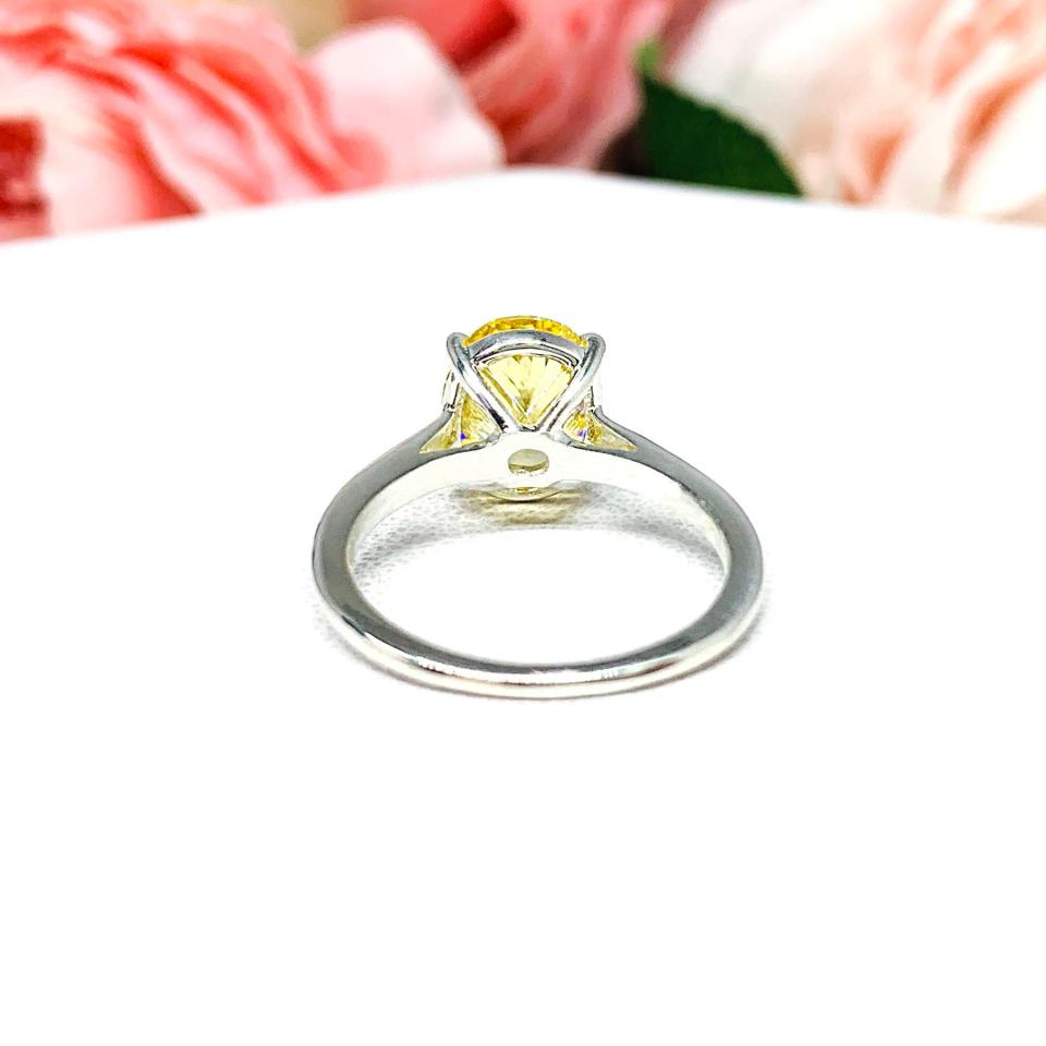 A sterling silver claw prong solitaire cathedral engagement ring featuring a well-faceted, canary yellow 10x8mm cz. Shown on a white surface with a pastel floral background.