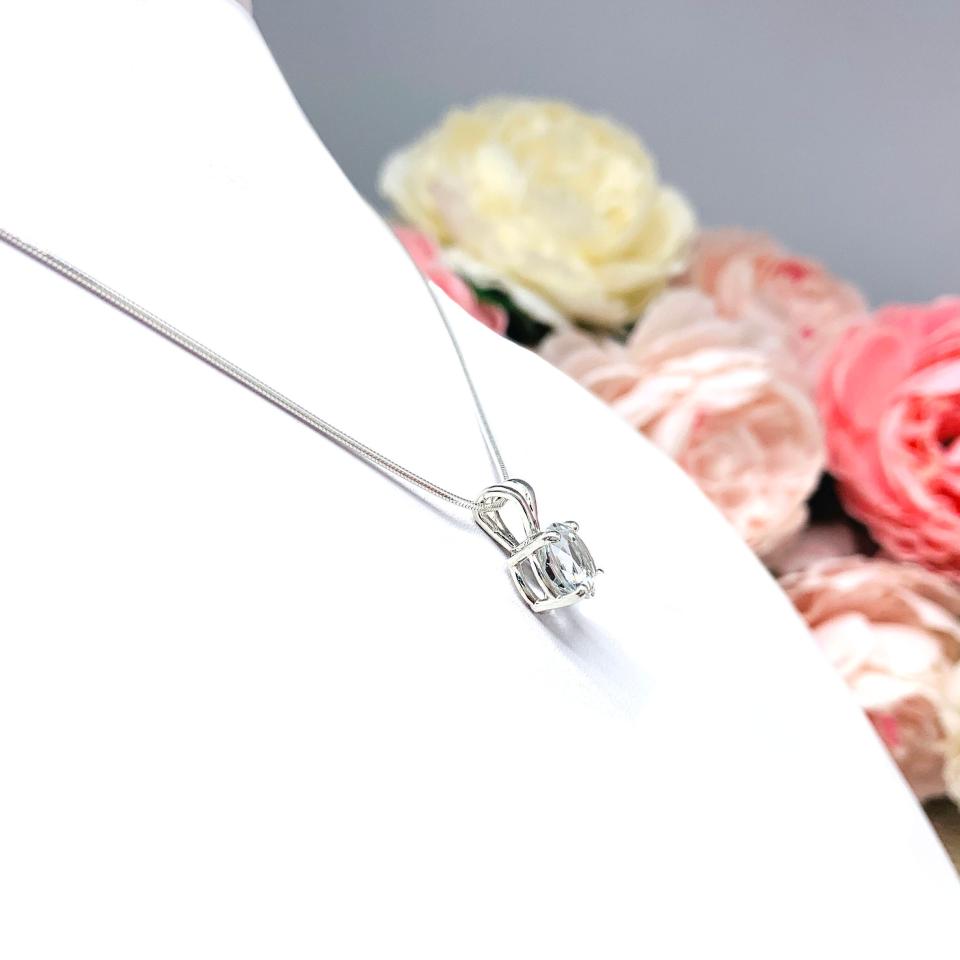 Sterling silver necklace featuring a round-cut white topaz pendant in a four-prong setting, suspended from a delicate silver chain. The natural gemstone is available in six size options and displays brilliant sparkle against a white background.