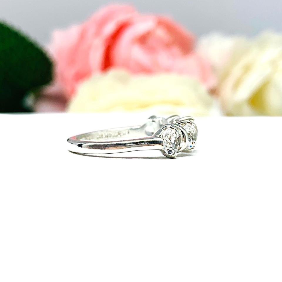 A sterling silver ring featuring five 4mm round white topaz gemstones in a row. The ring has rounded bars separating each stone. Displayed on a white surface with pastel floral background.