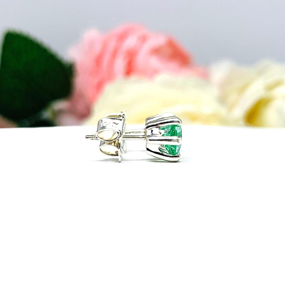 A pair of silver 6 prong earrings set with 6mm round sea foam green lab spinels, displayed with both earrings facing to the right to showcase the centrally located posts and butterfly friction clasps. The earrings are shown on a white background.
