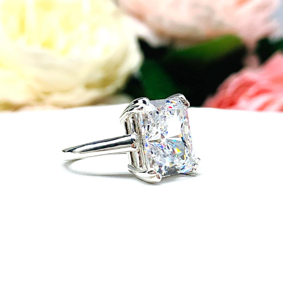 Elegant sterling silver cathedral engagement ring set with a large radiant cut cubic zirconia, beautifully photographed against a romantic and timeless soft-focus floral background of pink and white blooms.