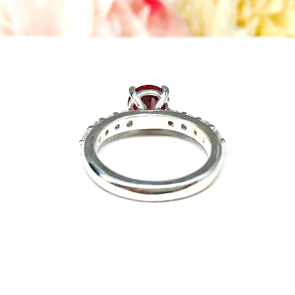 Sterling silver engagement ring with round lab-created deep red ruby and round CZ pave accents, shown on white surface.